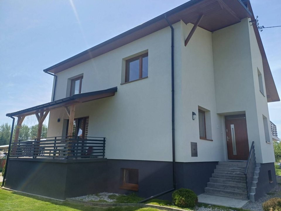 Dom jednorodzinny w Koprzywnicy po termomodernizacji — jasna elewacja, ciemny cokół i nowe drzwi